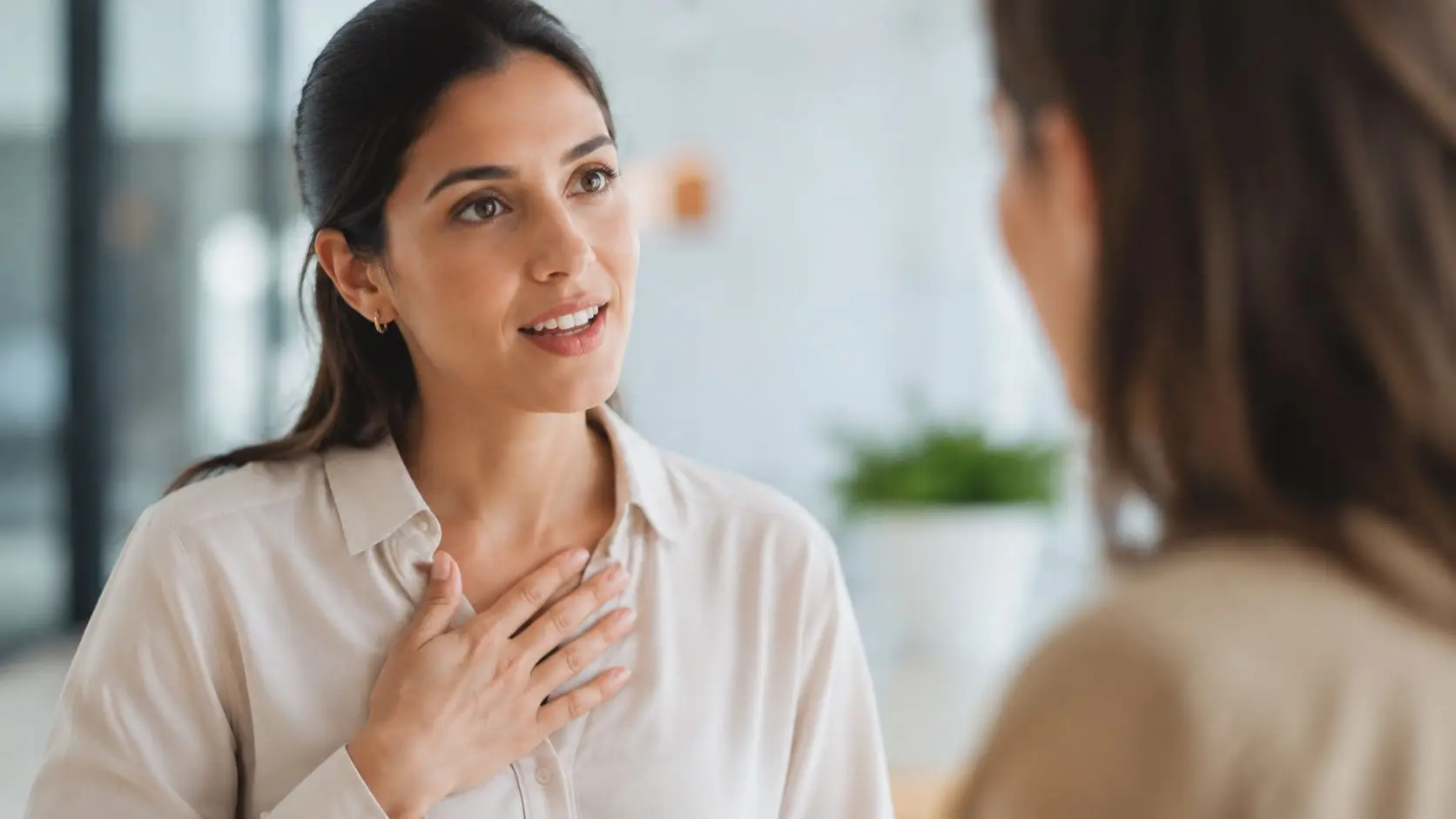 Una giovane donna con una camicia chiara comunica con entusiasmo tenendo la mano sul proprio petto